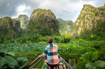 Woman traveling by boat on river amidst the scenic green karst mountains in Ninh Binh province, Vietnam