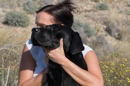 Woman sitting on ground cuddle and kiss Labrador dog while walking in nature.