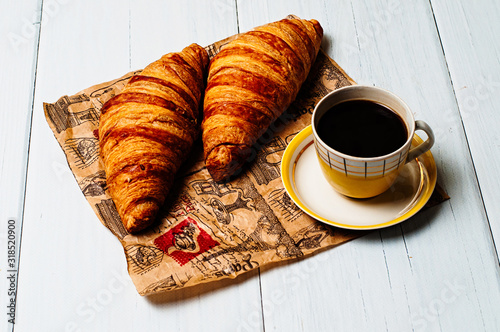 Fototapeta Naklejka Na Ścianę i Meble -  Espresso coffee in vintage yellow cup and saucer, croissants on craft paper, on a light background, breakfast concept