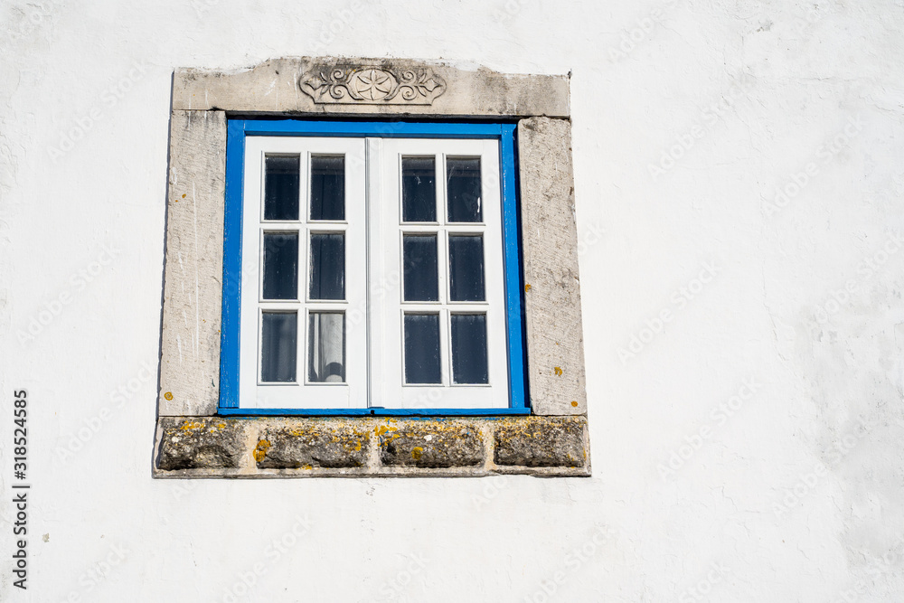 Old, ornate window with a painted blue frame and white wall. Traditional in Obidos, Portugal