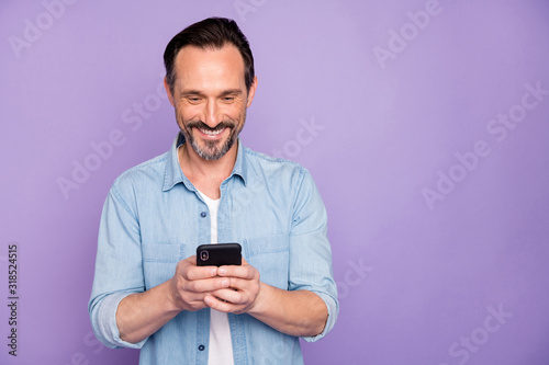 Portrait of positive cheerful man use smart phone chatting blog post follow bloggers share social media information wear good looking clothing isolated over violet color background