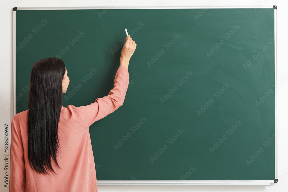 Female teacher writing on blackboard in classroom