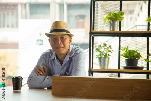 Close up relaxing Asian man in light blue shirt and hat cross his arms sitting at coffee shop.