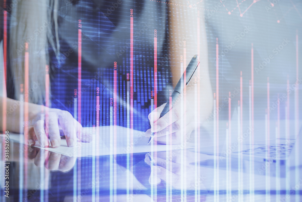 A woman hands writing information about stock market in notepad. Forex chart holograms in front. Concept of research. A woman hands writing information about stock market in notepad. Forex chart holograms in front. Concept of research.