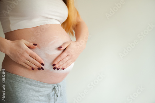 A pregnant woman is applying cream to her stomach for stretch marks. Pregnant tummy, oil for skin elasticity. Pregnant cares for her stomach on a gray background close-up and copy space.