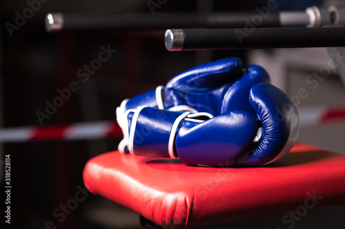 Close-up of a pair of blue Boxing gloves lying on a red chair outside the ring on a dark background. Selective focus.