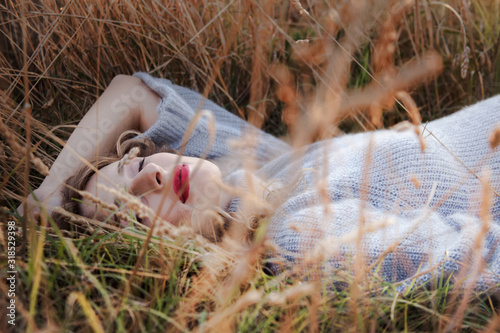 Young pregnant woman lied on the dried grass against the sunset. wiman holding the belly.  girl wearing fashion knitted sweater. the girl  care to be maternity photo