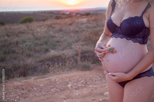 closeup of the belly of pregnant woman wearing underwear bra and lingerie. woman with love holding the abdomen outdoor against the sunset.