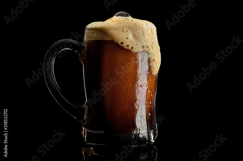 Fotografie Cold beer mug with black stout covered with drops and froth studio shot on black background