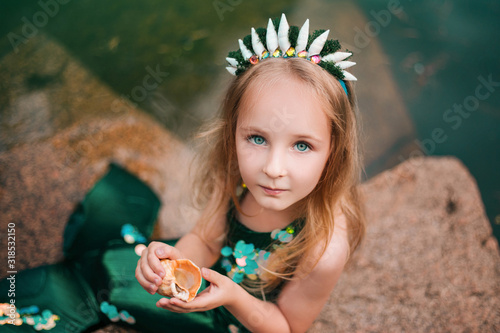 Obraz na plátně A little girl with white hair with a mermaid tail and shells is sitting on the shore