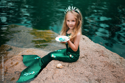 Foto A little girl with white hair with a mermaid tail and shells is sitting on the shore