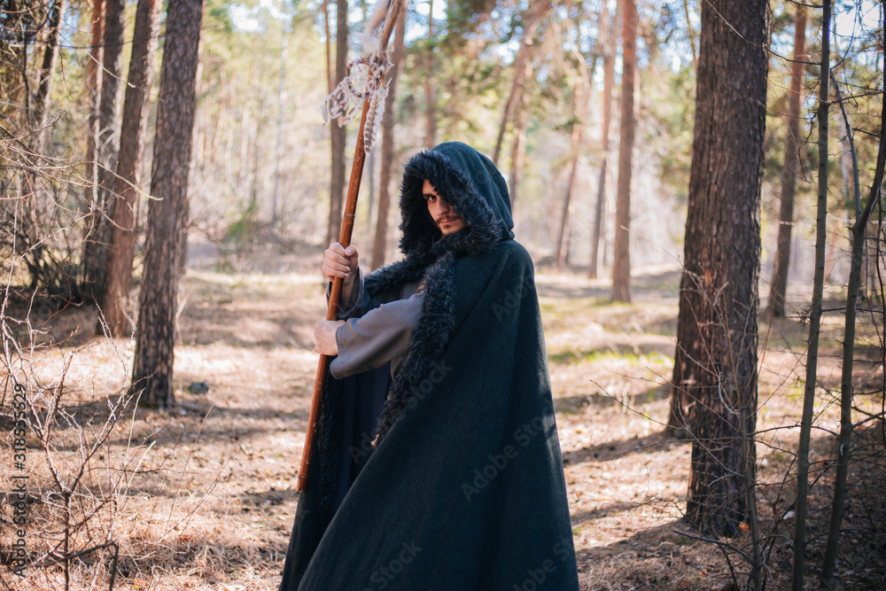 A man with a beard and a mustache in a robe and coat with a staff in his hand. A magician, a shaman conjures in the forest. Fantasy image A man with a beard and a mustache in a robe and coat with a staff in his hand. A magician, a shaman conjures in the forest. Fantasy image