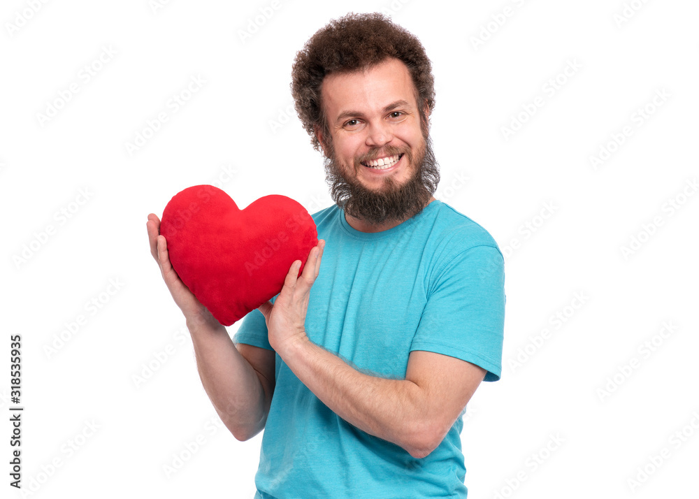 Happy Valentines Day. Crazy bearded Man with funny Curly Hair in blue T-shirt. Happy and silly guy in Love, isolated on white background. Portrait of Cheerful man with Red plush Heart, look at camera Happy Valentines Day. Crazy bearded Man with funny Curly Hair in blue T-shirt. Happy and silly guy in Love, isolated on white background. Portrait of Cheerful man with Red plush Heart, look at camera
