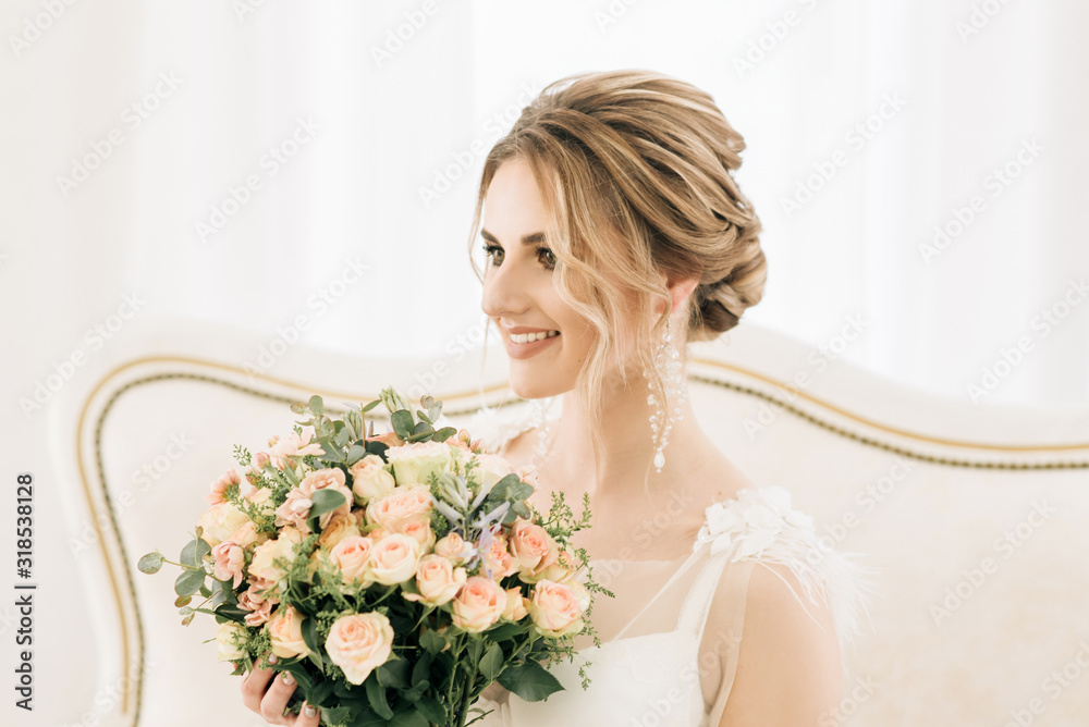 Naklejka premium Portrait of a beautiful young bride in a bright room in a romantic atmosphere. Bride in a negligee with a wedding bouquet