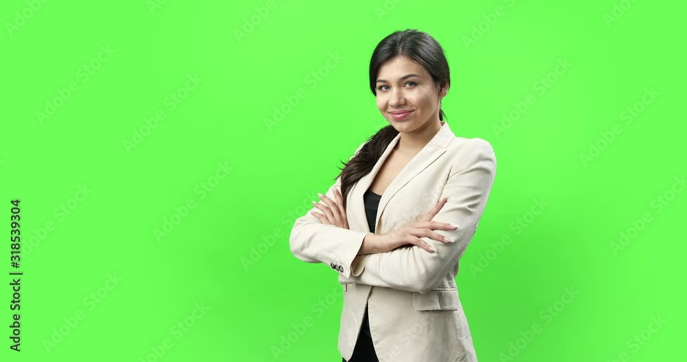 Confident young woman in eyeglasses and business suit posing with crossed arms on green chromakey background. Beautiful lady with dark hair smiling and looking at camera Confident young woman in eyeglasses and business suit posing with crossed arms on green chromakey background. Beautiful lady with dark hair smiling and looking at camera
