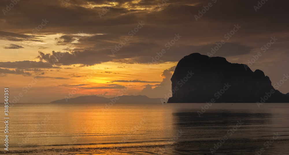 view seaside evening of mountain on the beach with orange and red sun light in cloudy sky background, sunset at Pak Meng Beach, Trang Province, southern of Thailand.
