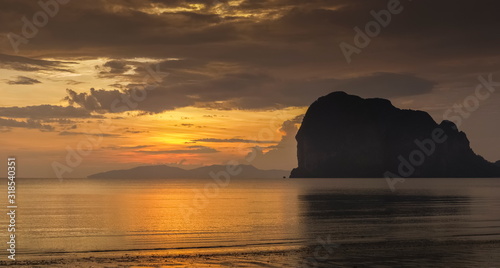 view seaside evening of mountain on the beach with orange and red sun light in cloudy sky background, sunset at Pak Meng Beach, Trang Province, southern of Thailand. © Yuttana Joe