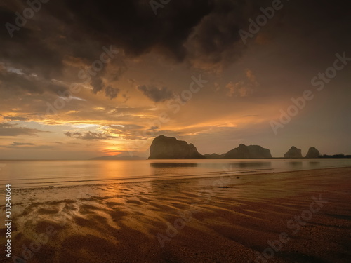 view seaside evening of mountains on sand beach with yellow sun light and dark clouds moving in rainy sky background, sunset and raining at Pak Meng Beach, Trang Province, Thailand.