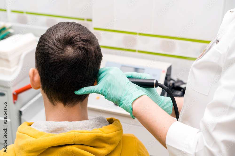 Preventive inspection of a teenage boy in a medical facility. Otorhinolaryngologist doctor pediatrician. Inspection of the sinuses of the ear with the reflector of the forehead and the nasal mirror Preventive inspection of a teenage boy in a medical facility. Otorhinolaryngologist doctor pediatrician. Inspection of the sinuses of the ear with the reflector of the forehead and the nasal mirror