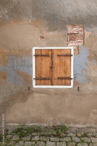 Closed window with wooden shutters on a weathered conctrete wall and old brick street in a grunge old look photo