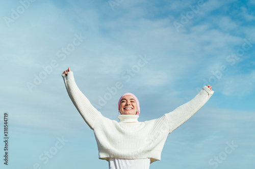 Portrait of happy young woman with cancer with arms up