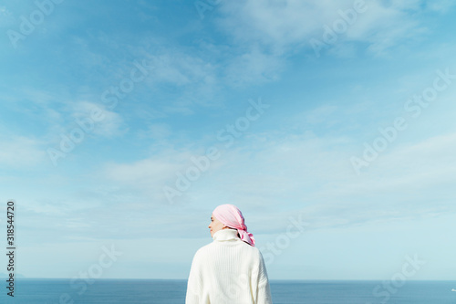 Back view of young woman with cancer looking to left on the coast