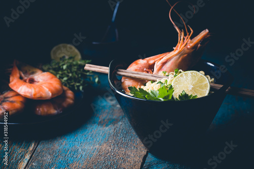 A bowl of instant Chinese noodles with green onions, red hot chilli peppers, and shrimps on a dark rustic background