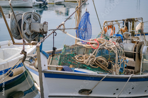 Close up of the fishing boats with marine winch and nets in the port of Roses. Mooring of the small fishing vessel at the dock. Fishing gear and equipment on the boat. Sunny day, calm sea.