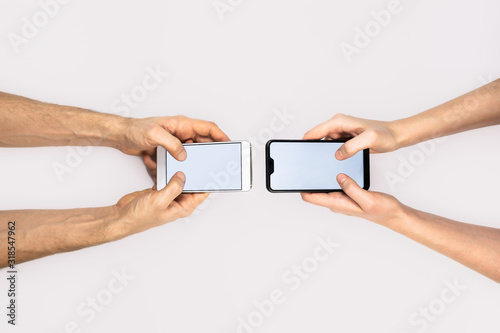 Female and male hands hold smartphones on white background with copy space. Messaging, texting, communication concept