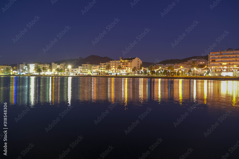 Panoramic view on seaside town and calm sea on a dramatic night sky background. Beautiful, amazing, great night over the bay of Roses, Catalunya, Spain. Reflections on the water.