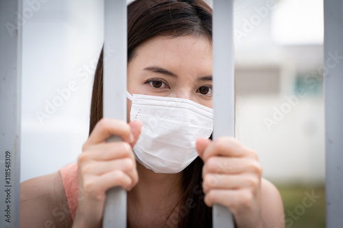 Woman feeling sick, wearing protective mask, behind bars in a jail.