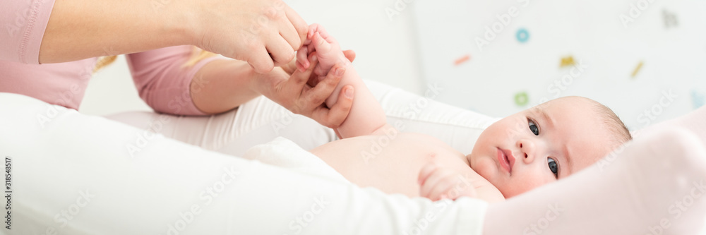 Baby massage banner. Mother gently massaging her baby boy while applying body lotion to his skin. Baby lying on back and looking at camera.