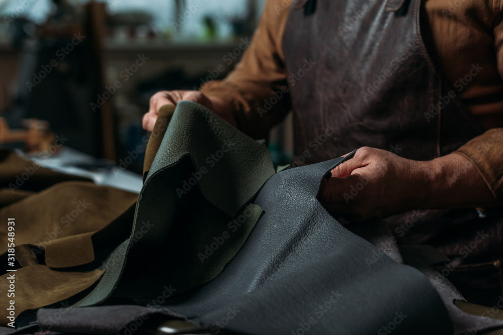 Obraz premium partial view of shoemaker holding piece of genuine leather in workshop