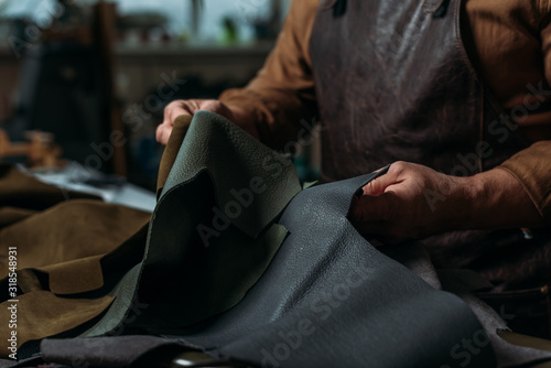 partial view of shoemaker holding piece of genuine leather in workshop