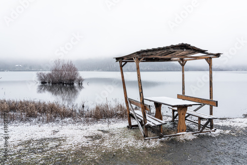 Snow covered table and benches in an empty public cafe by the lake photo