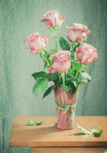 bouquet of pink roses on a light green background in a pink vase on a wooden table