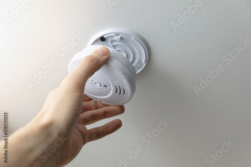 hand installing smoke detector on the room ceiling photo