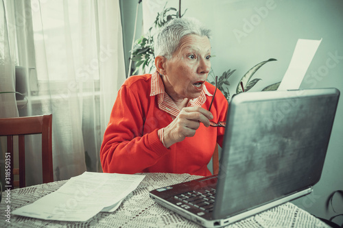 Old lady in disbelief, checking her laptop and papers