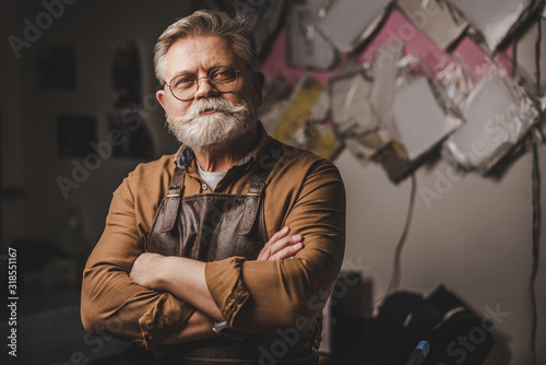 Foto positive, bearded cobbler standing with crossed arms and smiling at camera