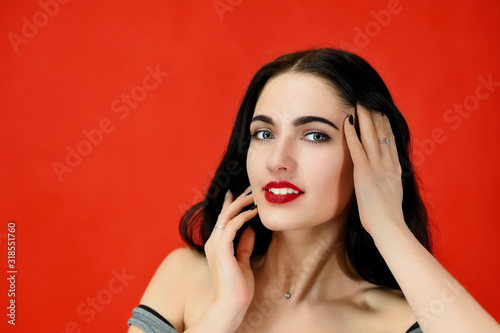 The concept of excellent makeup and cosmetics. Close-up Portrait of a pretty brunette model girl with excellent makeup and luxurious hair on a red background in the studio.