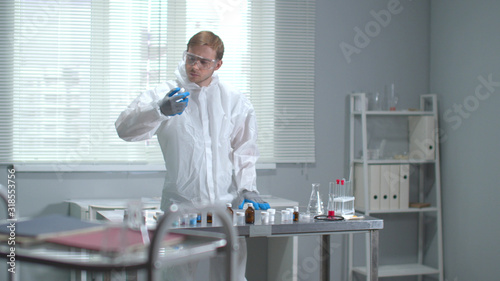 Man in protective workwear glasses and medical gloves check tubes in the laboratory