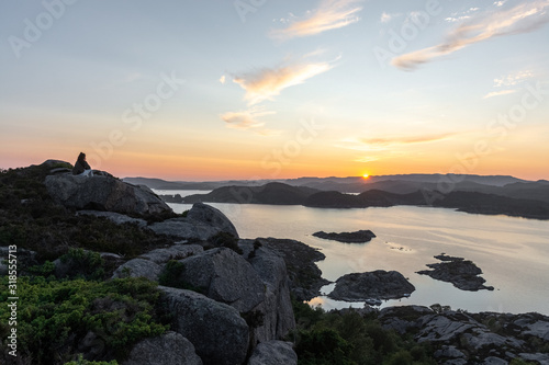 unknown woman on top of a rocky mountain overlooking the sea. Sunset is warming the sky. High dynamic range and mega panorama