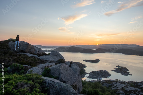 unknown woman on top of a rocky mountain overlooking the sea. Sunset is warming the sky. High dynamic range and mega panorama