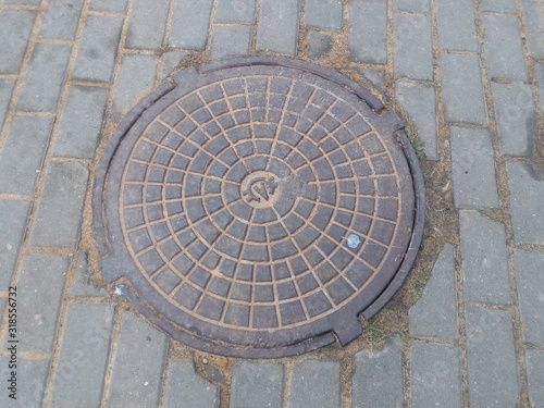 Cast iron manhole cover on the sidewalk made of tiles in the city