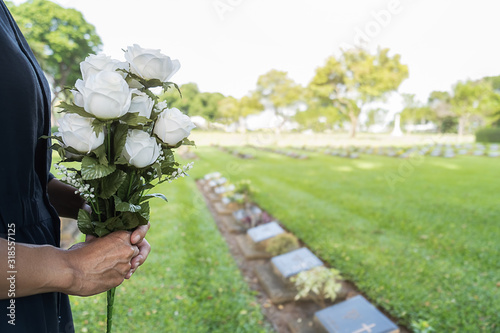 Mourning young woman holding white flowers at her family grave in beautiful green cemetery. photo