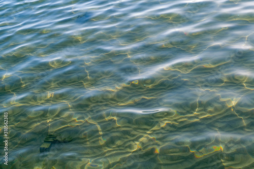 Clear sea water with sun glare in shallow and sandy bottom. Beautiful sun rays are reflected from the surface of the water.