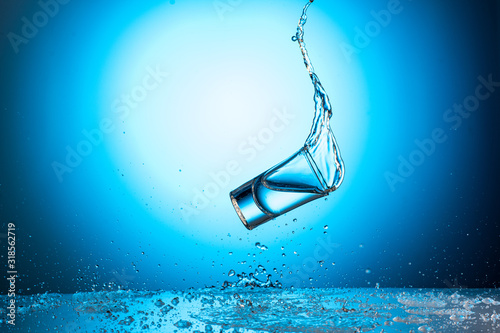 falling and jumping shot glass with a splash of water or vodka on a blue gradient background