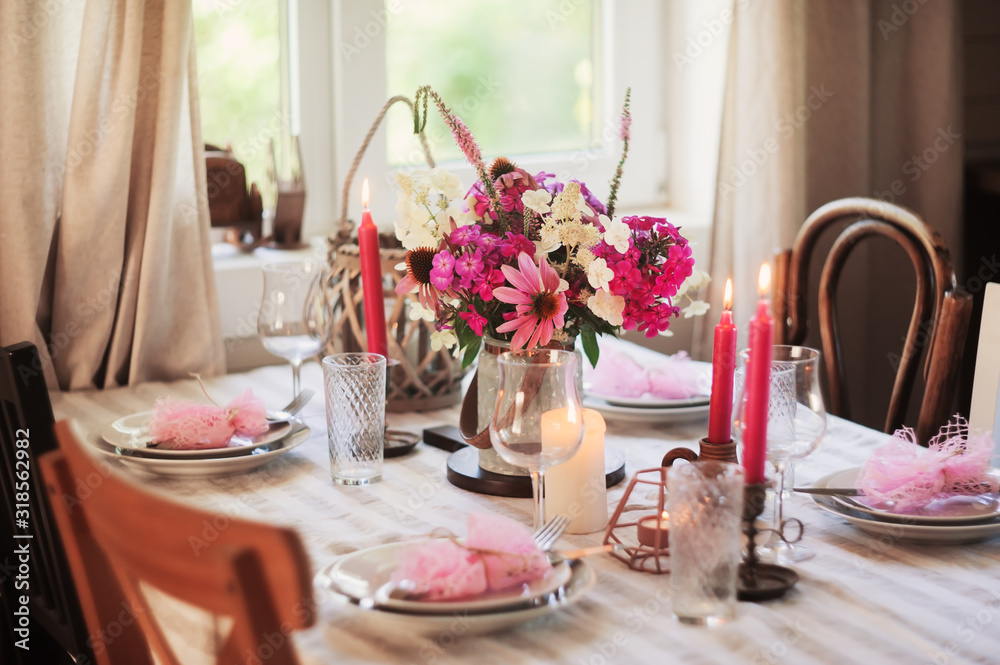 summer festive table setting in beautiful country house. Table decorated with pink flowers and candles.