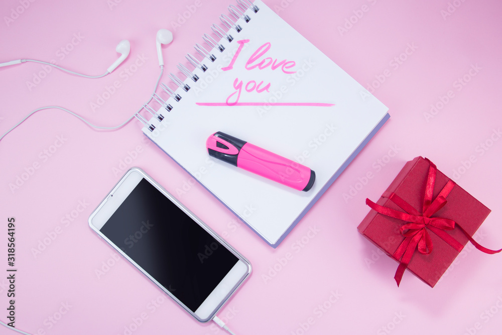 I love you with a marker in my notebook. Notepad, phone and gift are on a pink background I love you with a marker in my notebook. Notepad, phone and gift are on a pink background