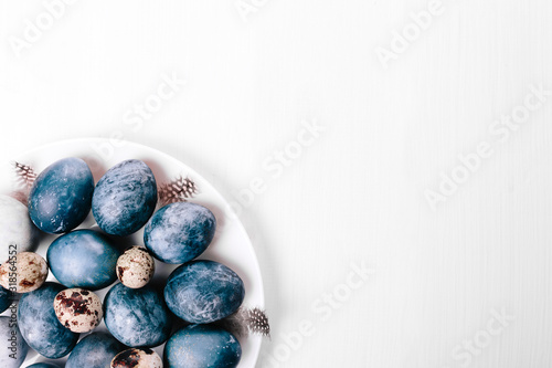 Beautiful group ombre blue Easter eggs with quail eggs and feathers on a white wooden background. Easter concept. Border eggs. Copy space for text. Classic blue color of year 2020
